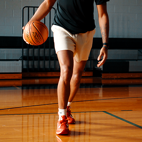 Male Model dribbling Legacy TF-1000 in cream colored shorts, black shirt and red shoes. 